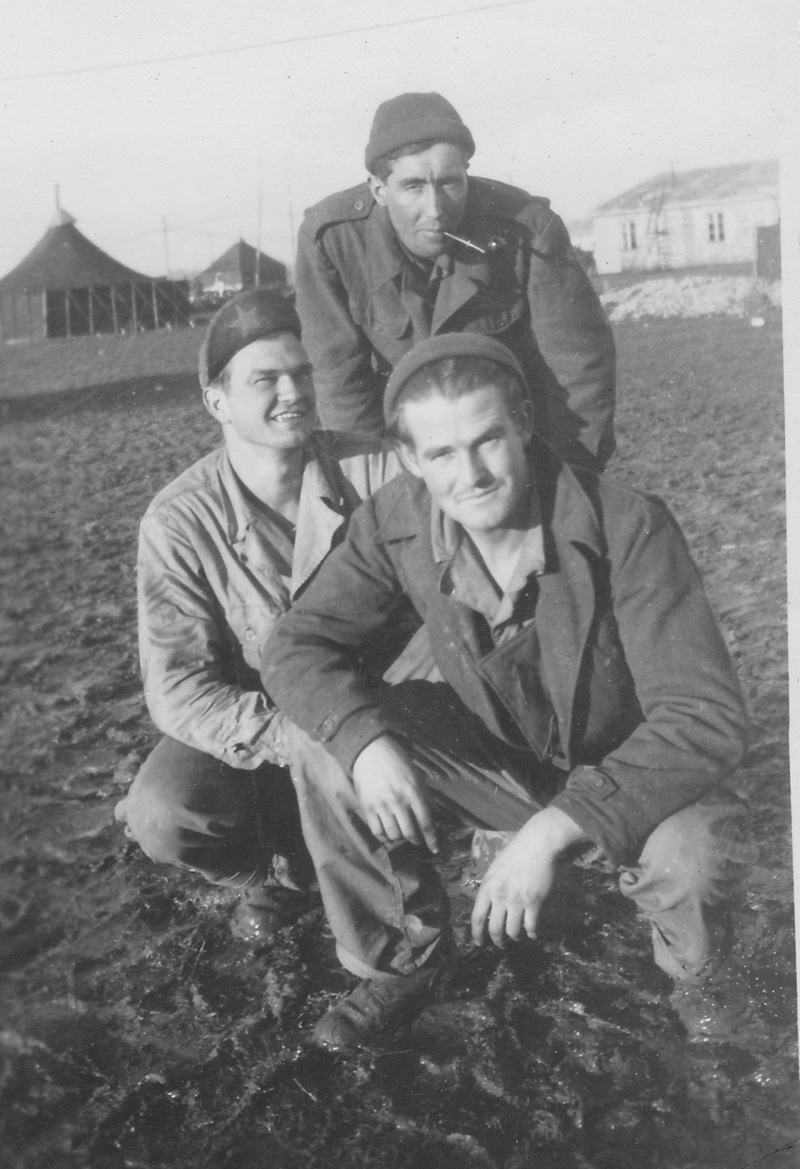 Three ground crew at the unknown airbase with tents and buildings in background